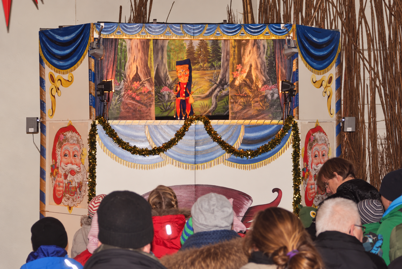 Kinder schauen Kasperle auf der weihnachtlich geschmückten Puppentheaterbühne zu